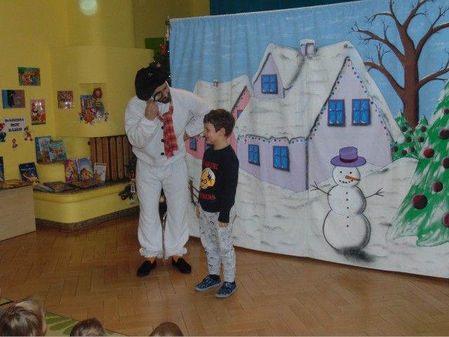 Chłopiec i ubrany na biało aktor na tle namalowanego na tkaninie domku pokrytego sniegiem, obok domku bałwan