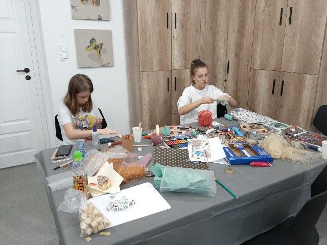 Dwie dziewczyny siedzą przy stole z materiałami plastycznymi i tworzą prace 